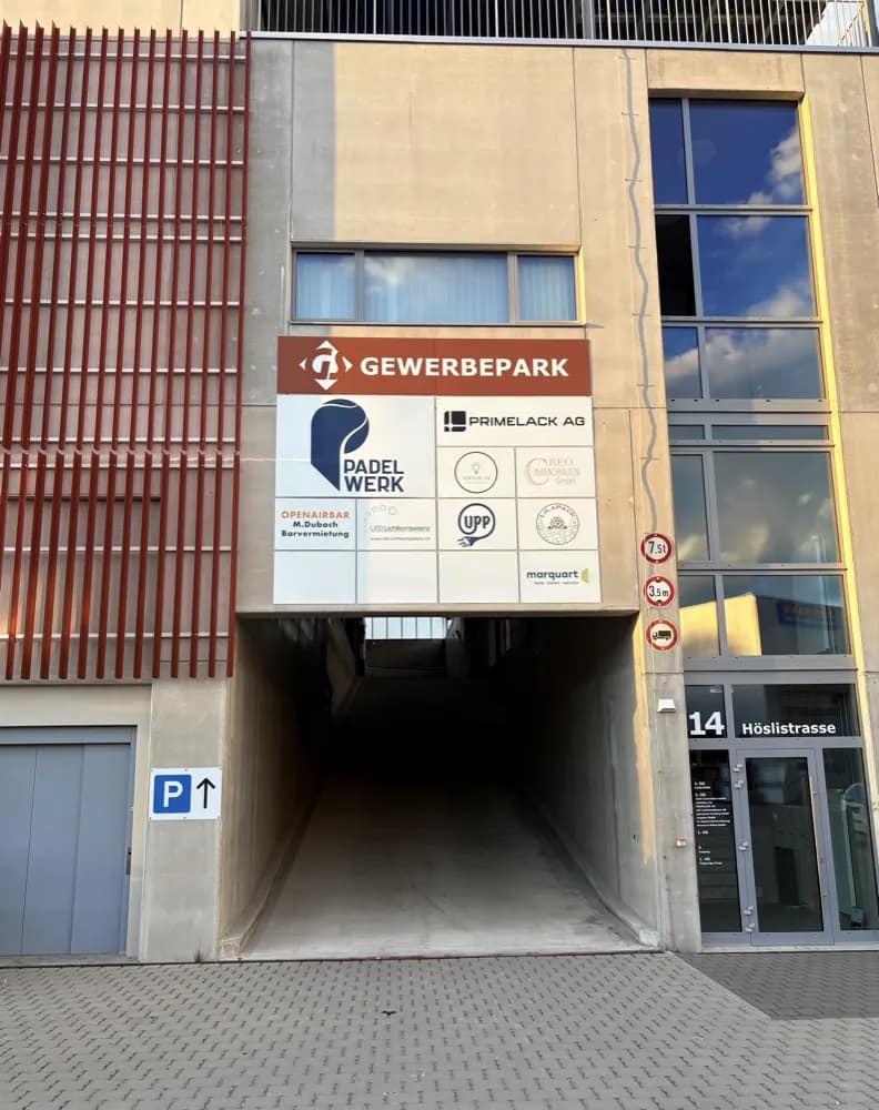 Die Einfahrt zur Tiefgarage an der Höslistrasse 14, darüber die Firmenschilder des Gewerbeparks und links ein blaues Parkzeichen
