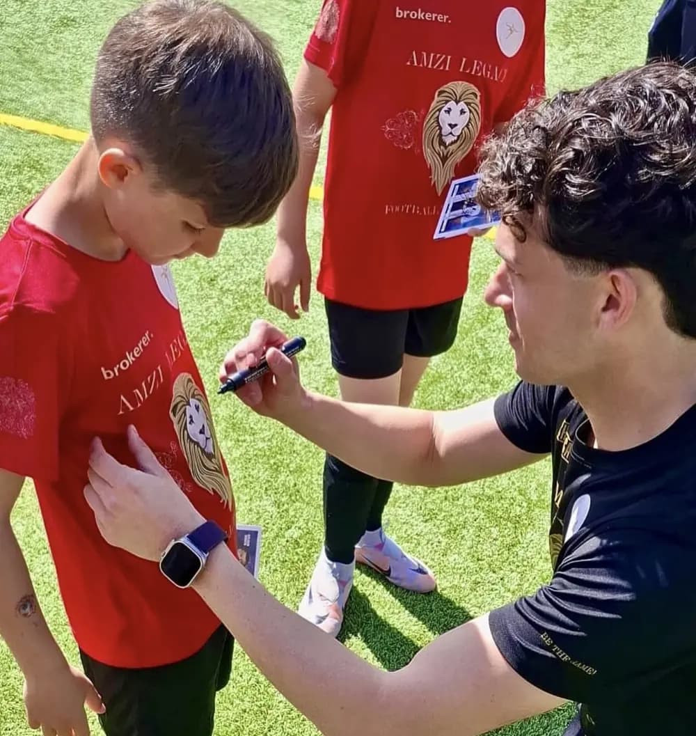 Ein Gast schreibt einem Jungen ein Autogramm auf das rote Trikot