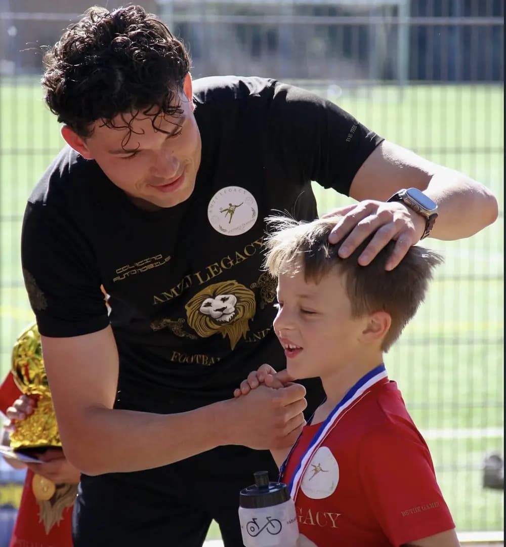Ein Trainer legt einem Jungen mit Medaille die Hand auf den Kopf, beide lachen