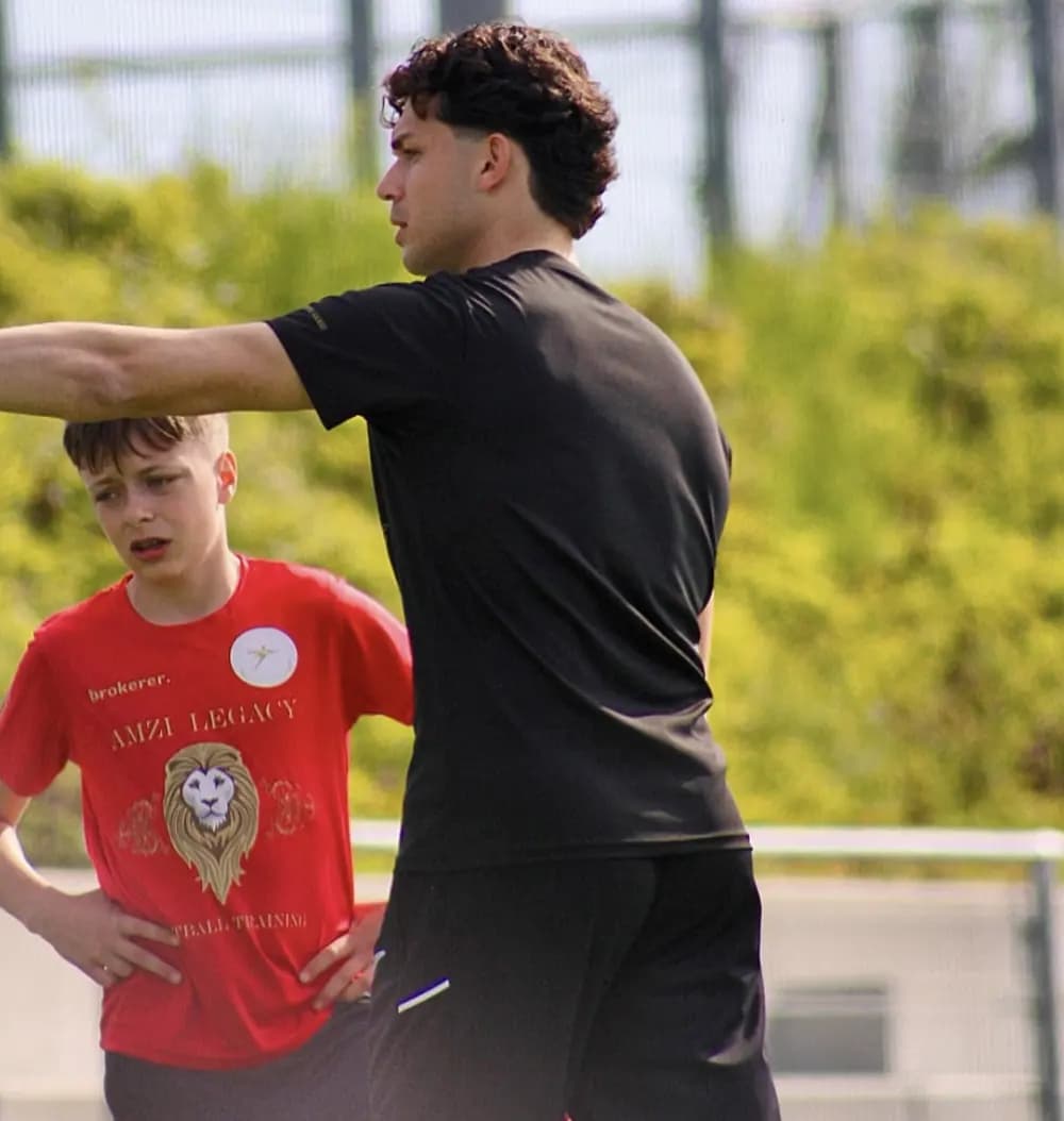 Ein Trainer erklärt einem Jungen im roten Trikot die Laufrichtung und zeigt mit dem Arm