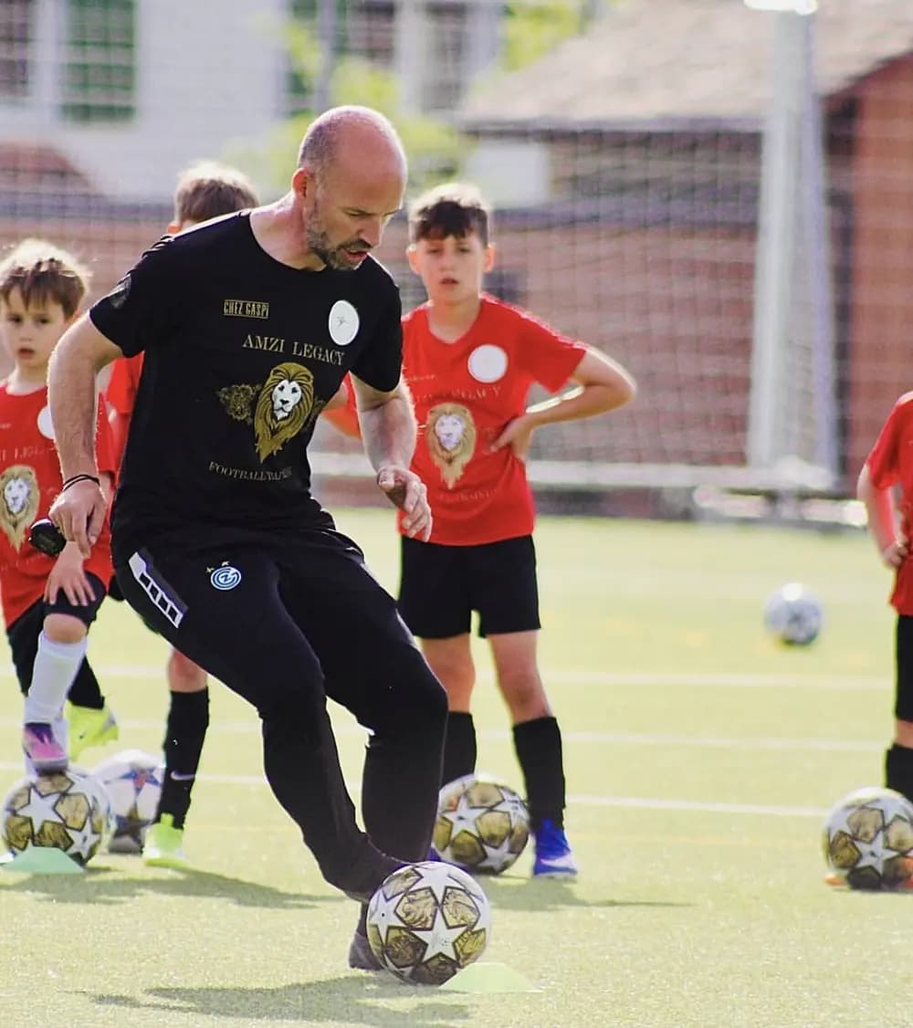 Ein Trainer führt eine Übung am Ball vor, dahinter warten zwei Kinder