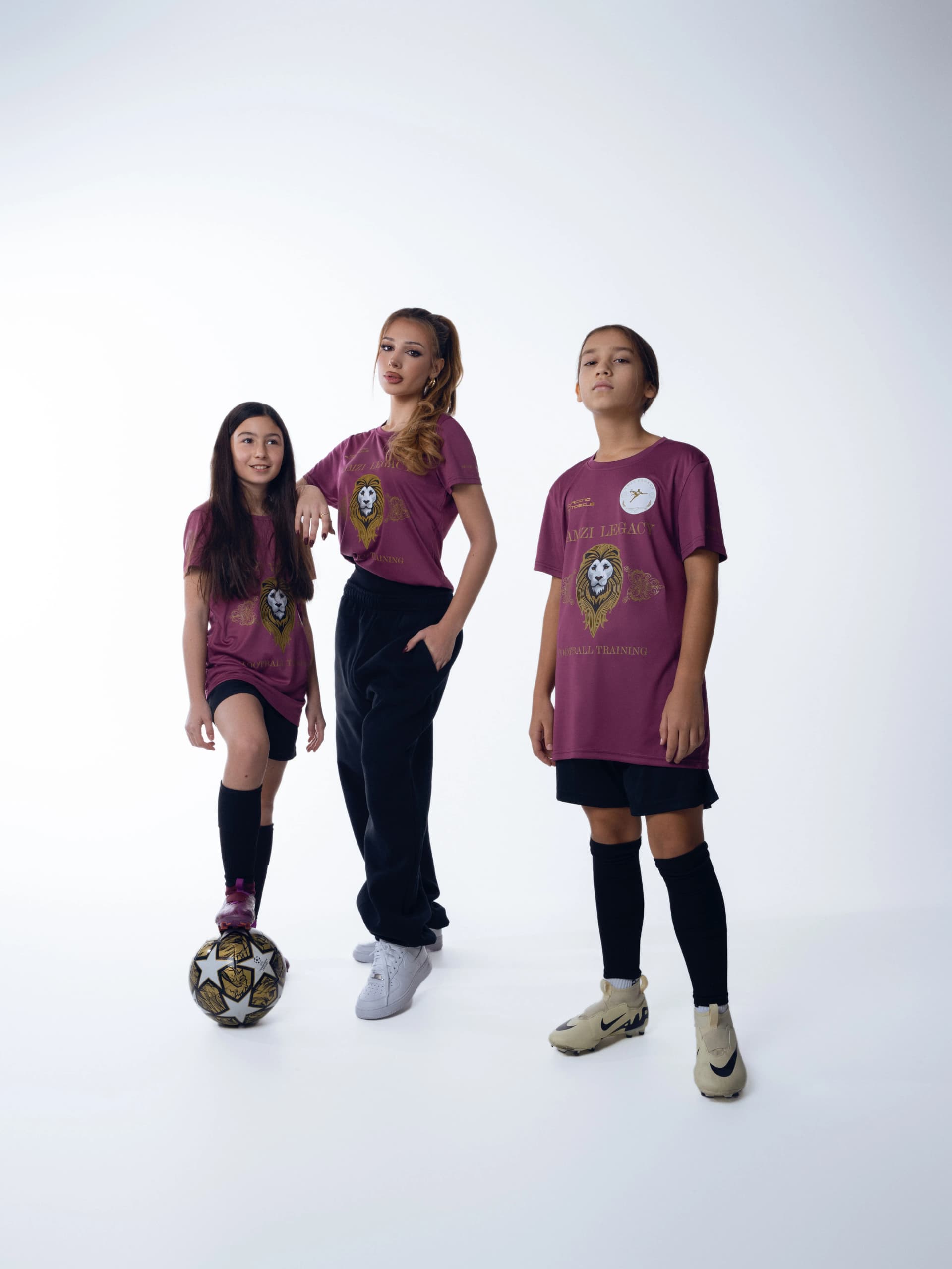 Drei Spielerinnen in weinroten Trikots, die mittlere mit dem Fuss auf dem Ball