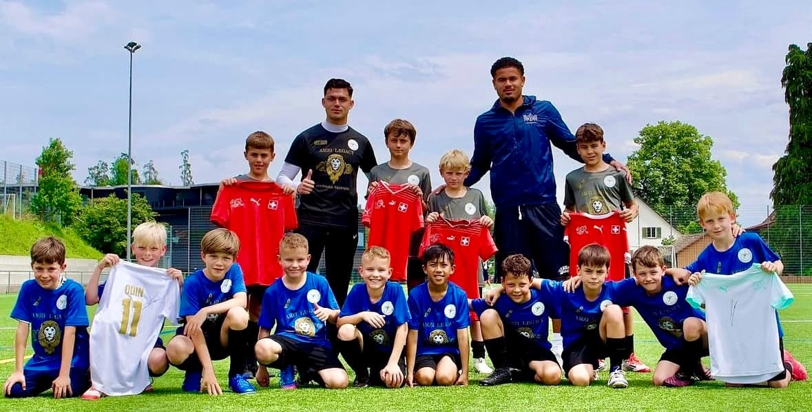 Die Kinder des Camps stehen mit Miralem Amzi und Simon Sohm auf dem Rasen, mehrere halten signierte Trikots hoch