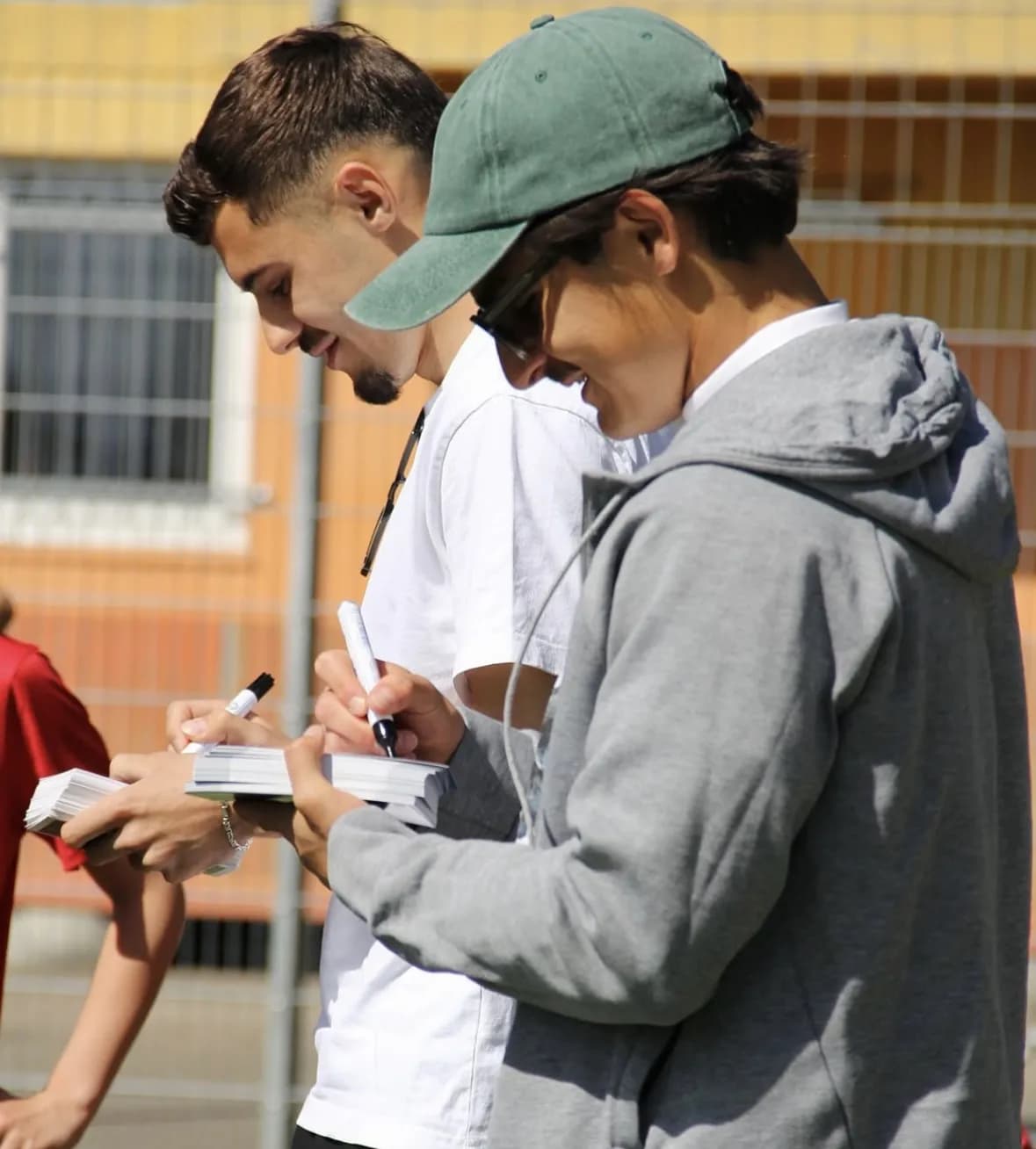 Zwei Profispieler schreiben mit Filzstiften Autogramme auf einen Stapel Karten