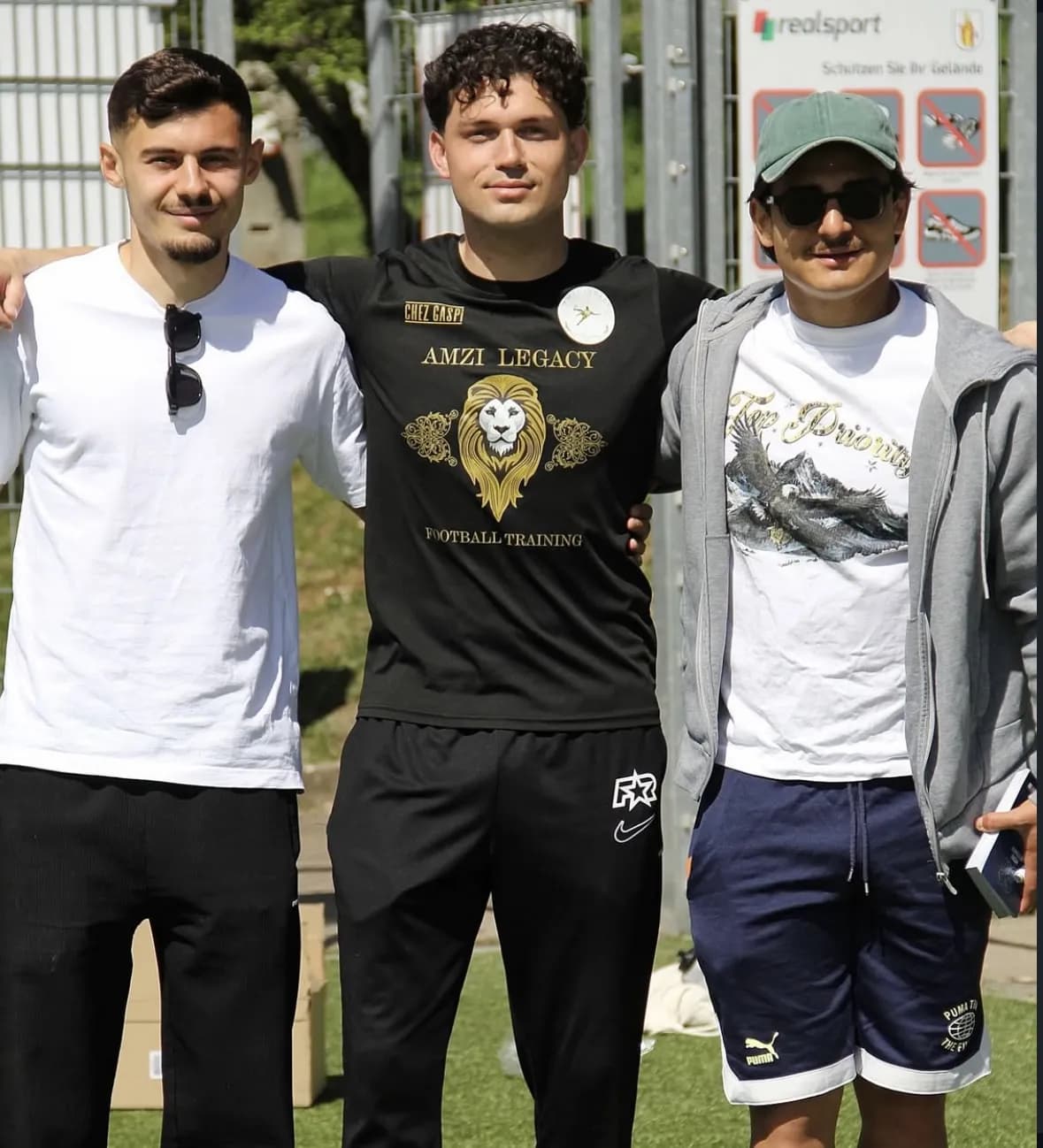 Miralem Amzi im Trikot von Amzi Legacy steht zwischen zwei Profispielern auf dem Rasen
