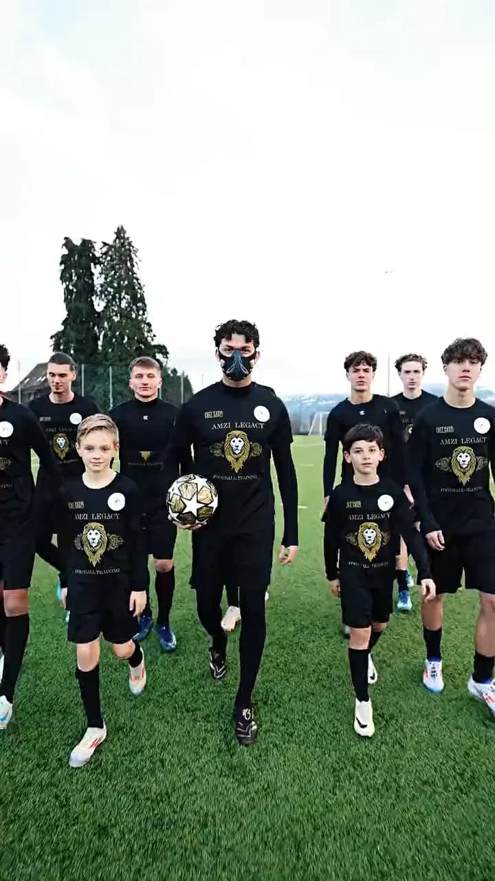 Die Mannschaft geht in schwarzen Amzi-Legacy-Trikots nebeneinander über den Rasen, Miralem Amzi in der Mitte mit dem Ball