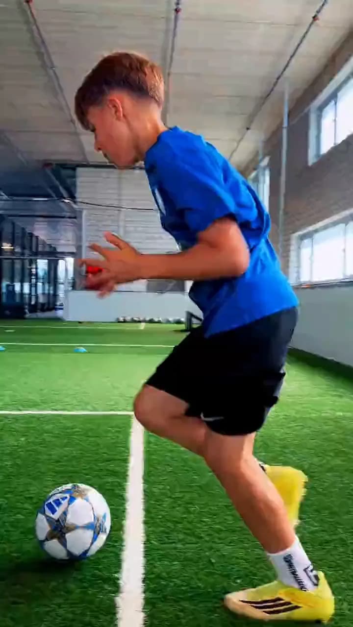 Ein Junge im blauen Trikot führt den Ball über den Kunstrasen der Halle